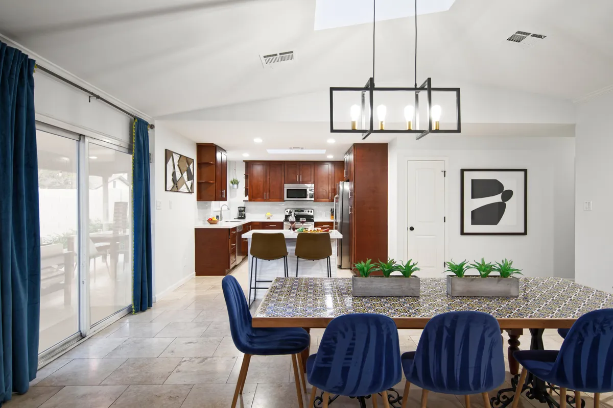 This image highlights the dining table adjacent to the kitchen, with stylish cabinetry, a distinctive light fixture, and a sliding glass door letting in plenty of sunlight. The decor is modern and inviting, setting the stage for group meals or casual conversations.