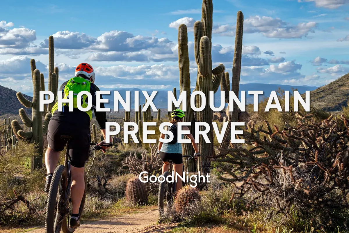 A dynamic exterior shot featuring a rugged mountain landscape dotted with towering cacti. In the foreground, bicyclists are seen traversing a scenic trail, capturing the spirit of outdoor adventure and exploration in Scottsdale’s desert terrain. The warm hues of the setting sun create a dramatic, inviting atmosphere.
