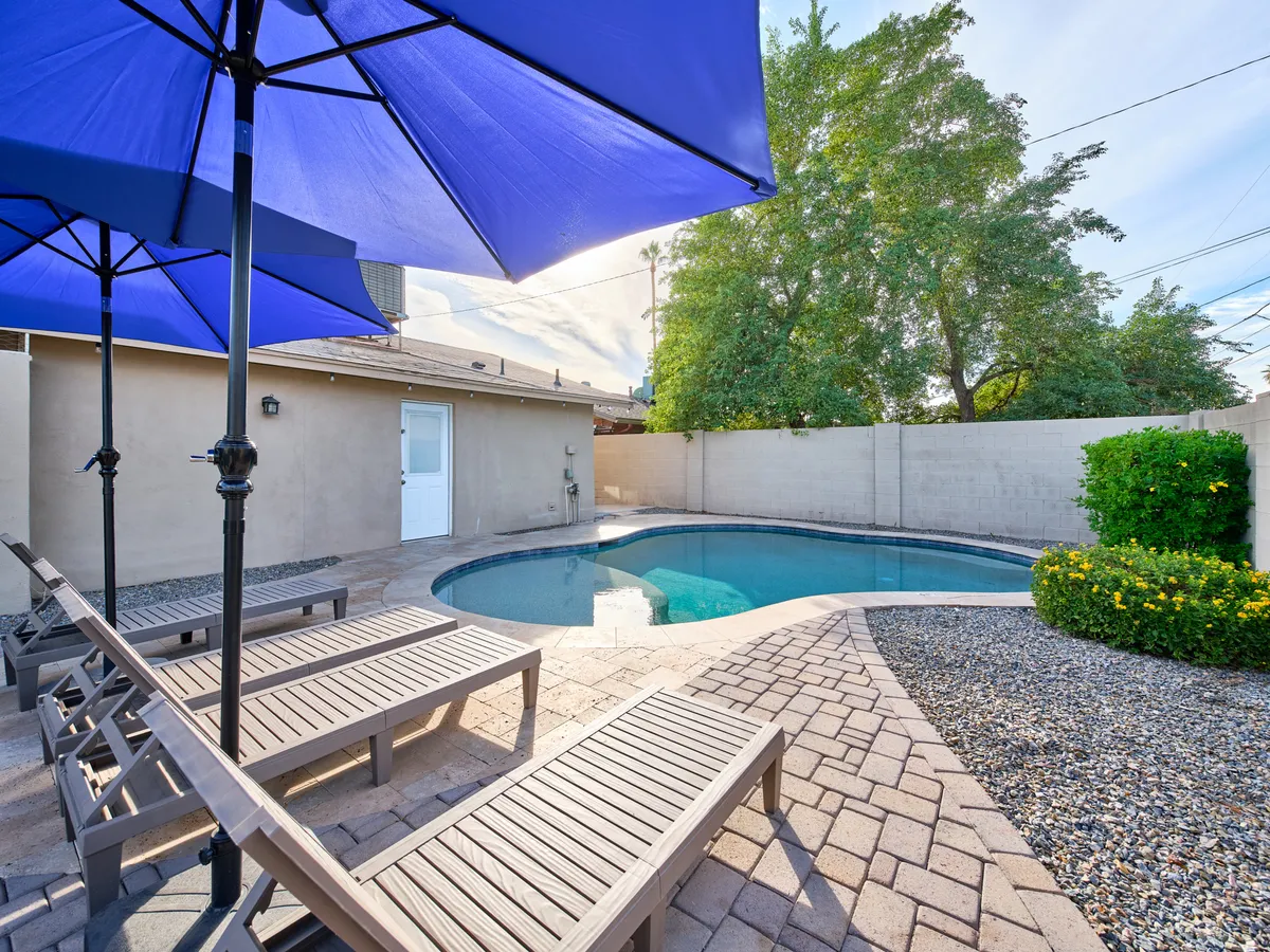 A sparkling swimming pool is surrounded by resort-style loungers and blue umbrellas, set amidst lush greenery. The tranquil scene suggests a perfect spot for morning swims, sunbathing, or relaxing with a cool drink.