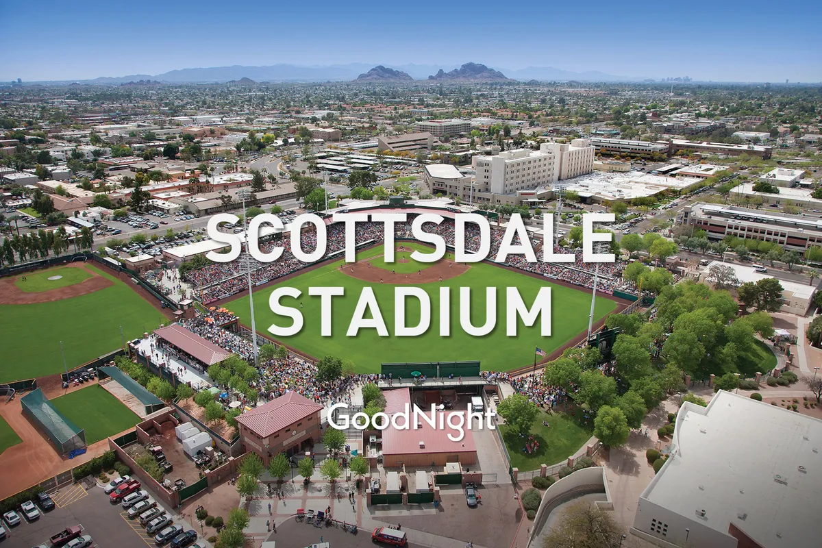 A vibrant baseball stadium filled with cheering fans, with the field in play and scenic mountains beyond. The atmosphere is festive, highlighting community spirit and live entertainment.