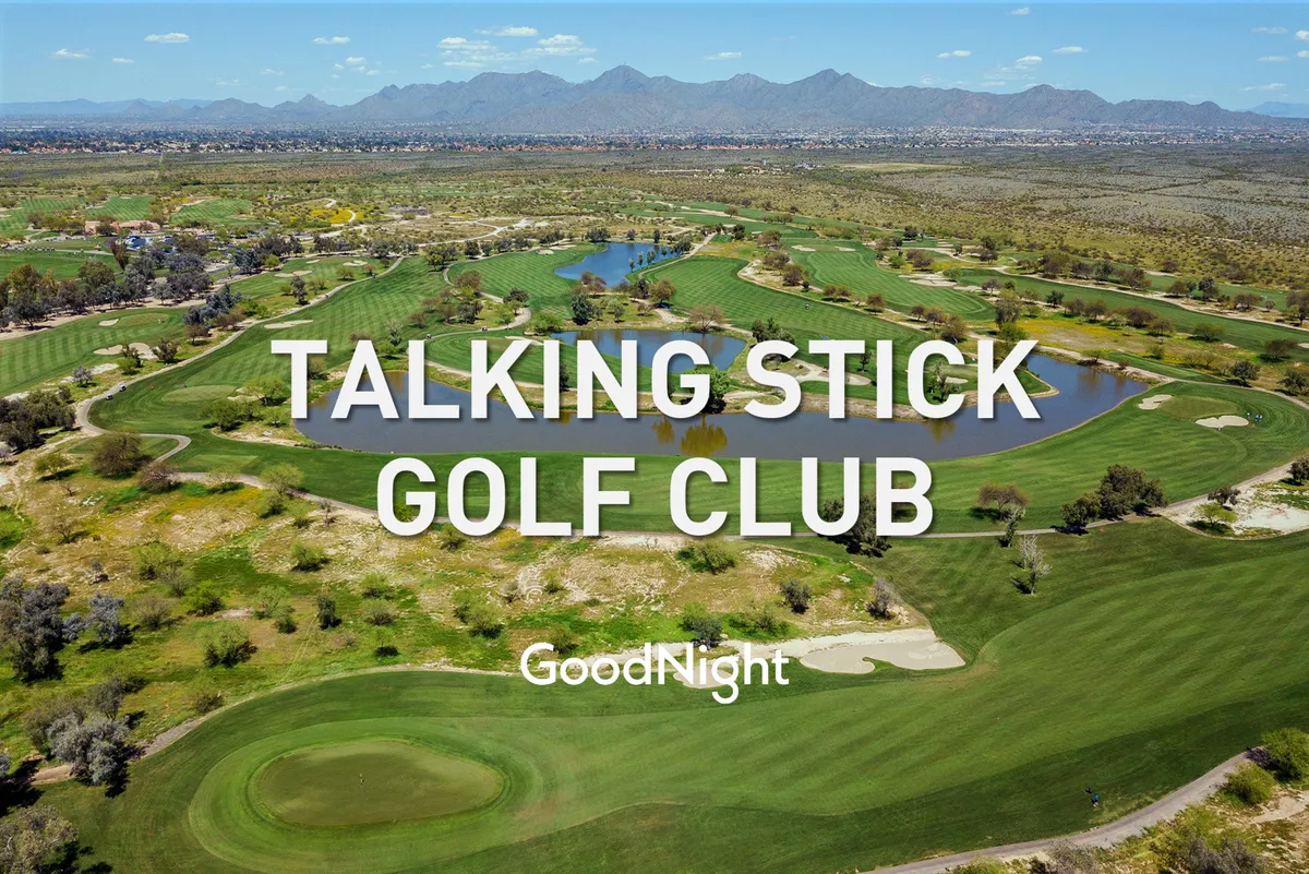 A sweeping view of a beautifully maintained golf course, with lush fairways, sparkling water features, and a dramatic mountain backdrop. The sun sets in the distance, casting golden light over the landscape.