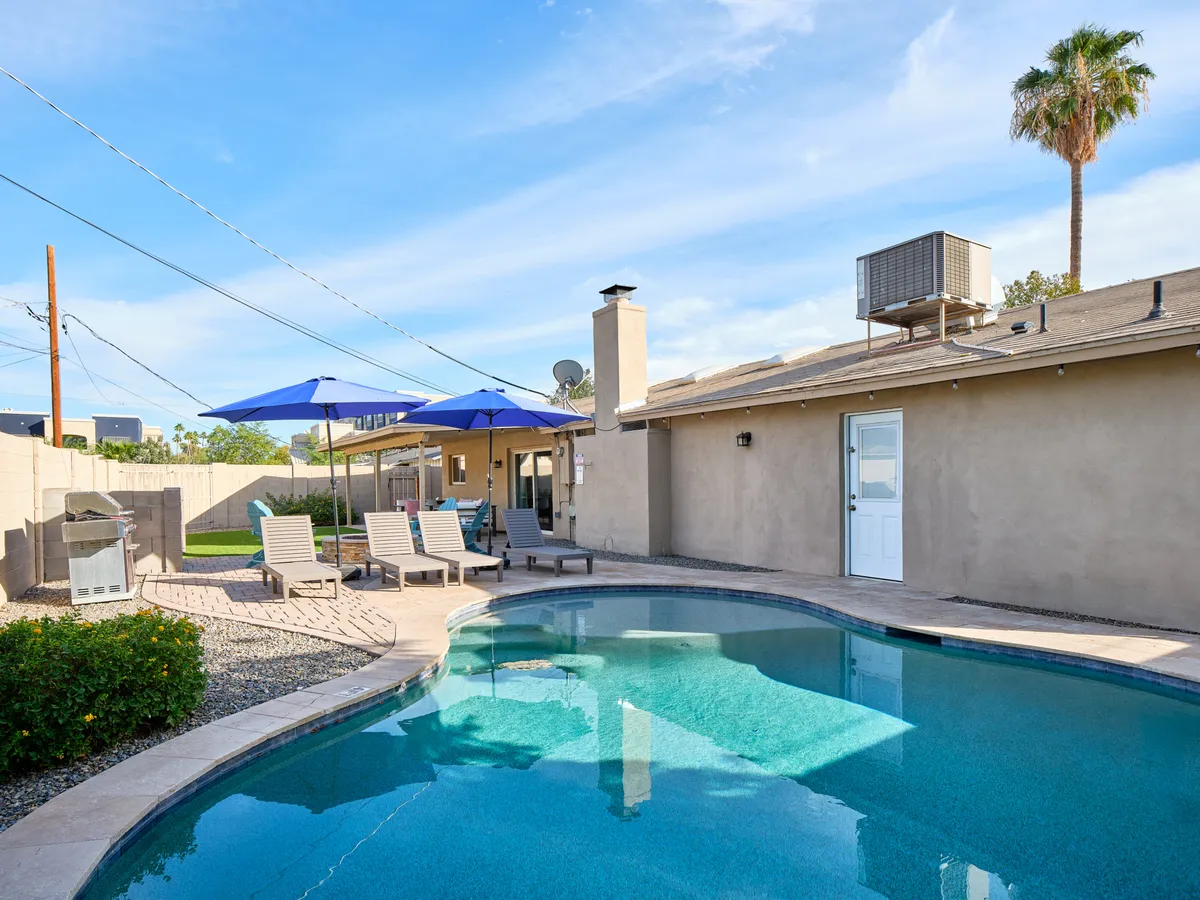 This exterior shot features a sparkling swimming pool with inviting lounge chairs, umbrellas, and an outdoor grill—perfect for relaxing or socializing with friends before heading out on the town.